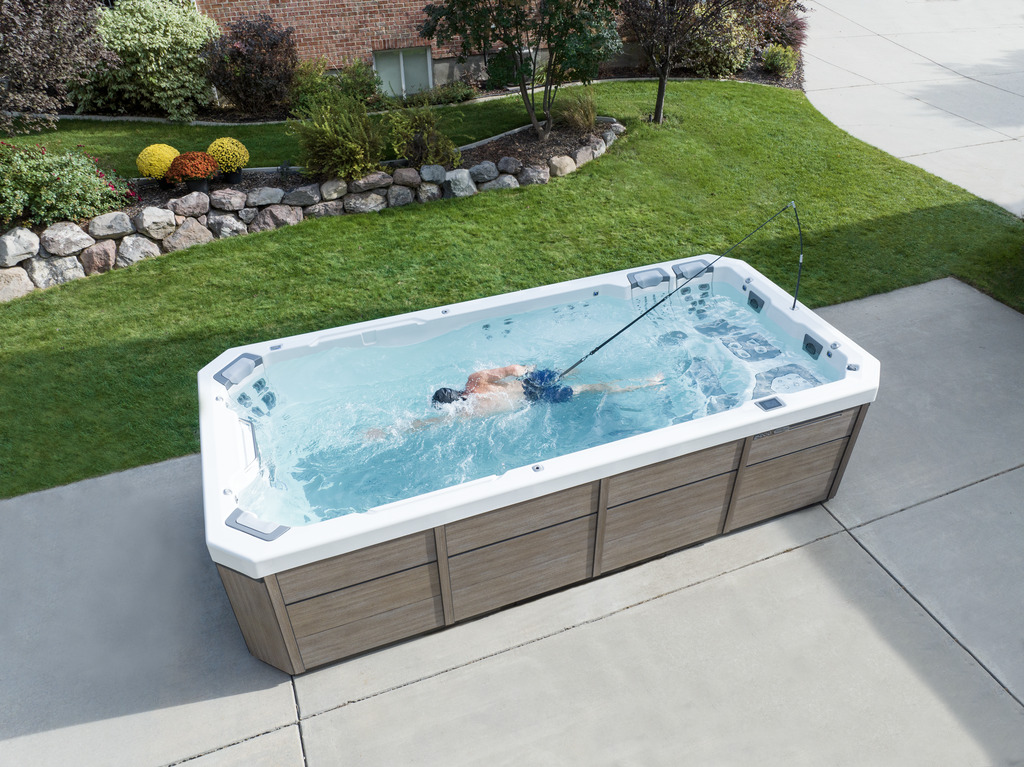 Swimmer using the current in a Bullfrog Swim Series spa on a backyard patio