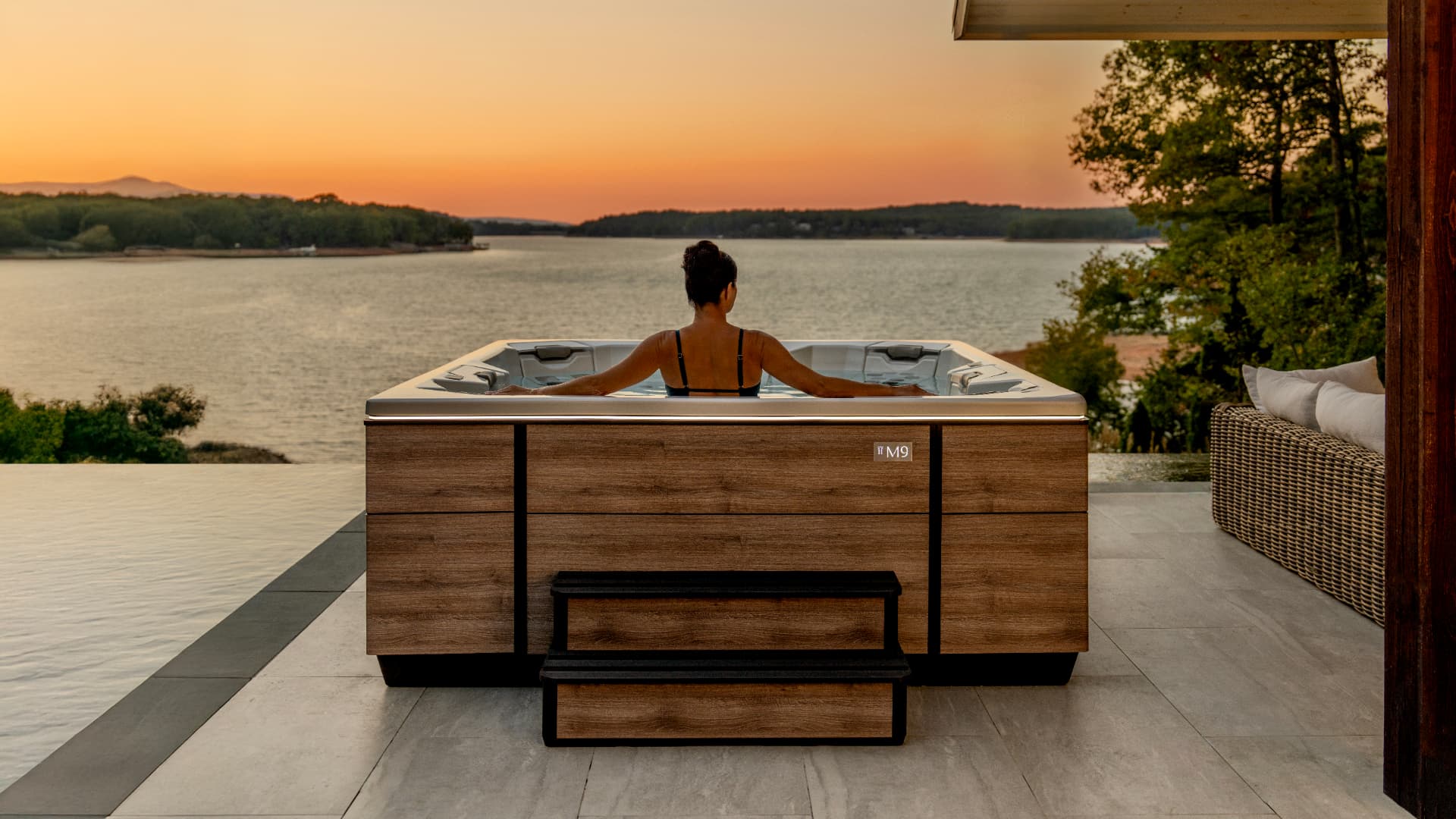 Woman soaking in a Bullfrog M9 spa overlooking a lake at sunset