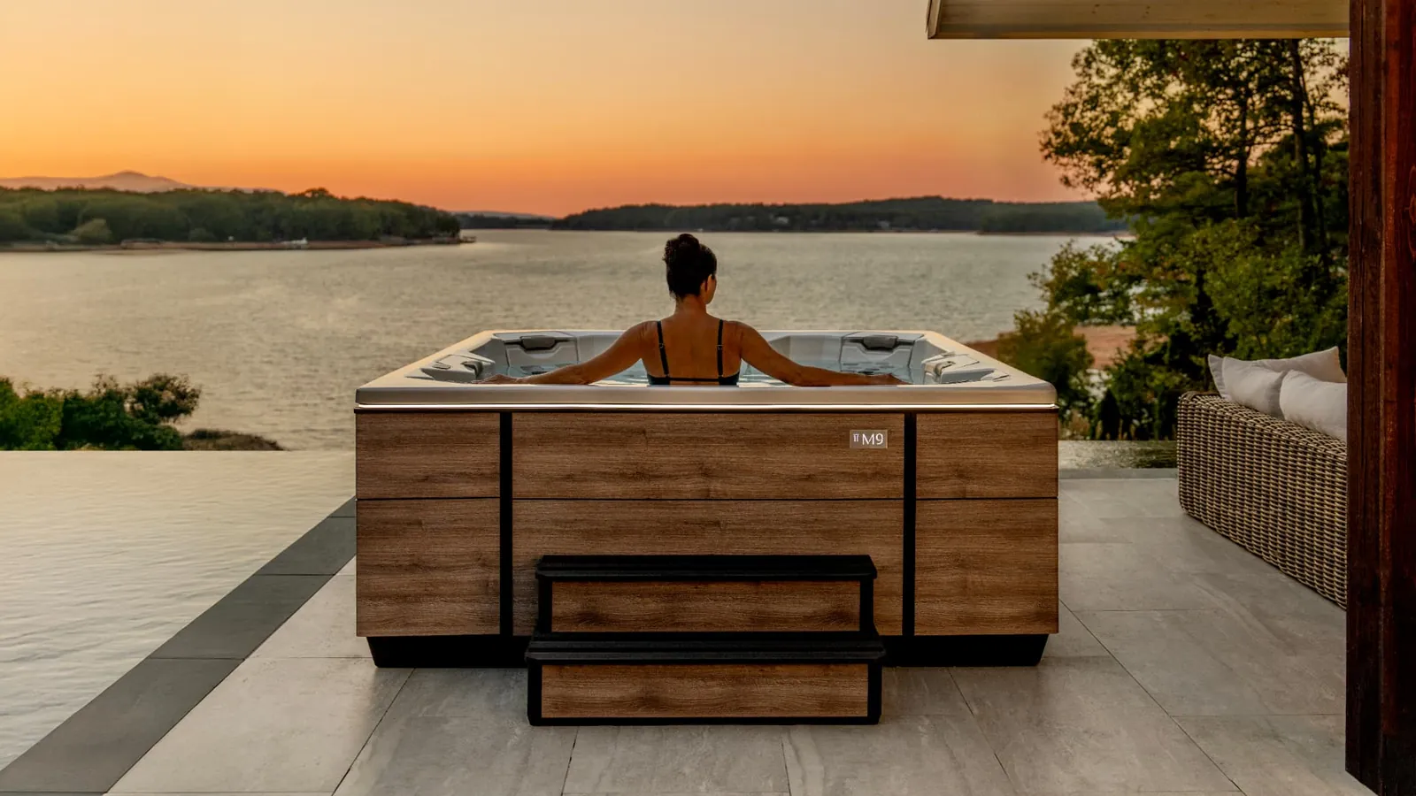 Woman soaking in a Bullfrog M9 spa overlooking a lake at sunset